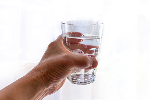 A hand holding a glass of water with a white background.