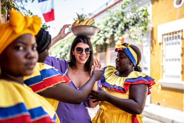 une touriste met un bol de fruits sur la tête avec des palenqueras dans la rue à carthagène, en colombie - food caribbean street cartagena photos et images de collection
