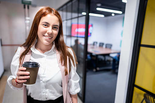 Portrait of a young woman standing holding coffee cup at office