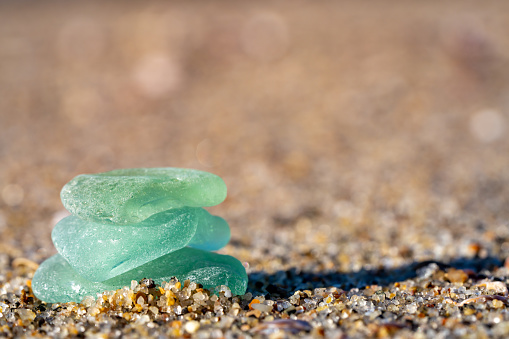 A stack of blue and green sea glass captured in the sand on a sunny day.