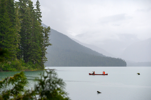 Couple canoeing on lake against beautiful mountain. Man and woman enjoying vacation in Whistler. View of stunning nature.
