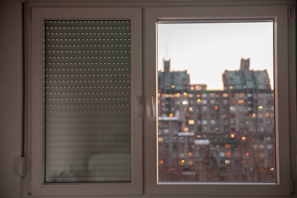 Selective blur on PVC windows, in plastic, one covered with roller shutters, in an urban environment of Serbia with residential high rise buildings in background.