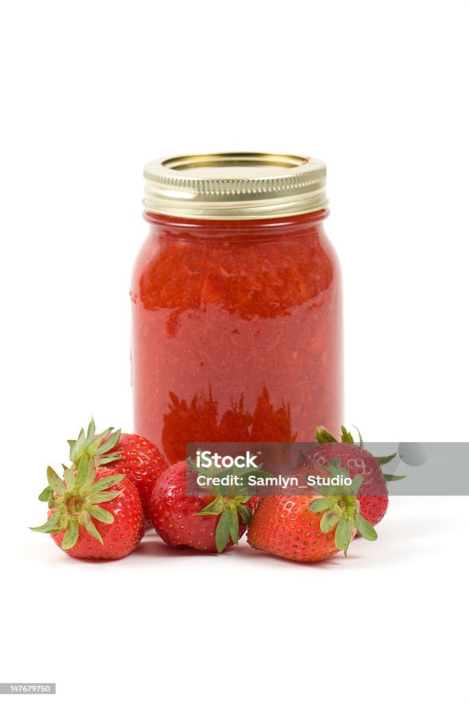 A jar of strawberry jam with strawberries besides it A jar of strawberry jam with strawberries in front. Berry Fruit Stock Photo