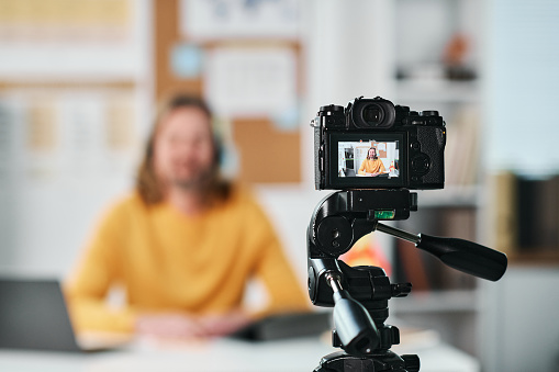 Mature man sitting at table in the classroom and recording lesson for his students on camera