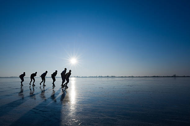 Six speed skaters skate outdoors on frozen water stock photo