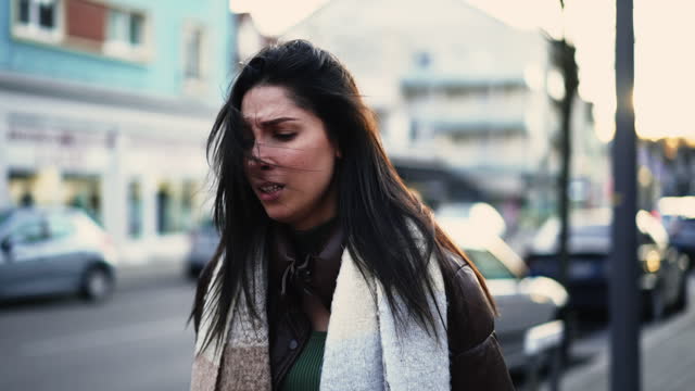 Worried young woman walks in street shaking head in disbelief. Preoccupied female person in 20s feeling frustration and stress during difficult times