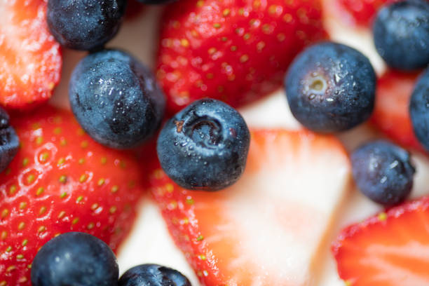 Close-up of frosty blueberries and raspberries in a red enamel mug with a blurred natural green background. Refreshing concept of healthy food and summer harvest.