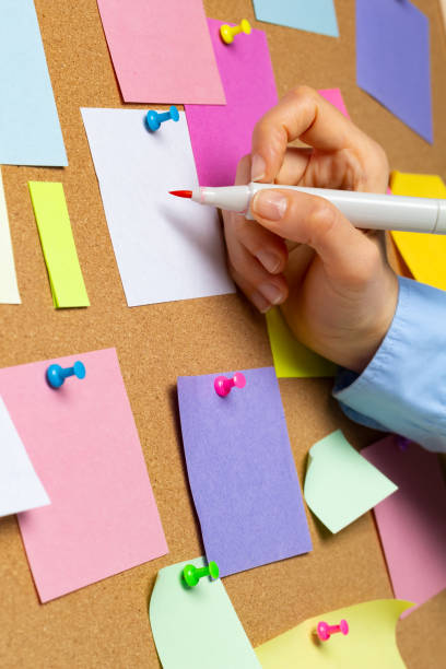 istock A business woman's hand writes on sticky notes attached to a cortical bulletin board. 1476810955