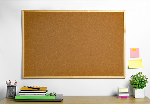 Empty cork board with wood frame over work desk. Place for notes and reminders.