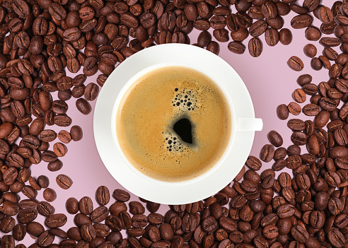 Cup of tasty espresso and roasted coffee beans on pink background, flat lay