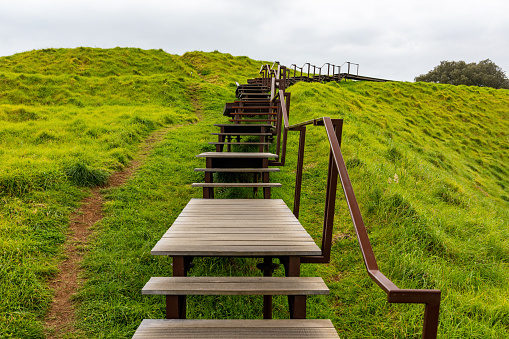 This 25 October 2022 daytime photo shows a boardwalk at Maungawhau Mount Eden in Tāmaki Makaurau Auckland. The steps appear next to a worn footpath along the rim of the ancient volcano in Aotearoa New Zealand. The boardwalk is part of an ongoing project to protect the historically significant land where a pā or fortified village once stood.