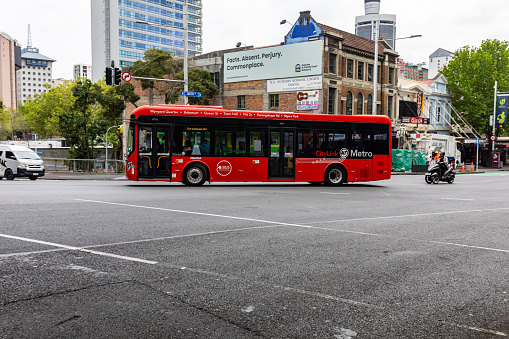 This 25 October 2022 daytime photo shows an AT Metro Bus in Tāmaki Makaurau Auckland, Aotearoa New Zealand. The red CityLink bus is an electric vehicle. This photo was taken at the intersection of Queen St and Mayoral Dr. Auckland Transport manages public transportation around the super city.