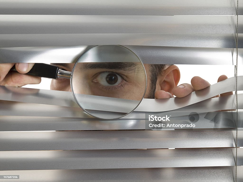 Extreme peeping Tom A man is peeping through the blinds with a magnifying glass. Window Blinds Stock Photo