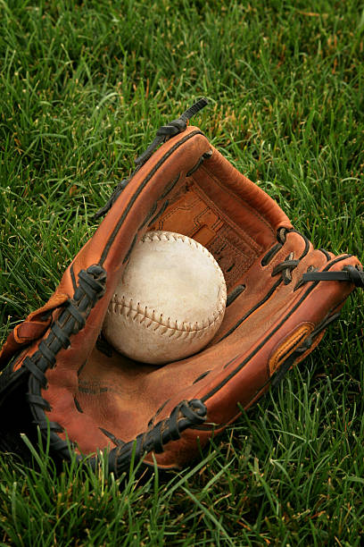 Studio shot of an old baseball resting near a catcher's mitt on grass.
