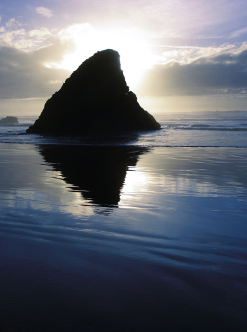 Sun setting behind a rock outcrop on a reflective beach landscape