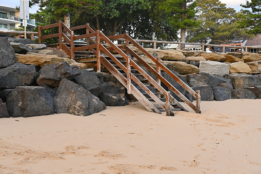 Wooden steps over an ocean retaining wall leading down to the beach