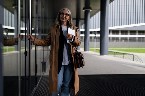caucasian senior businesswoman at the entrance to the office building with a laptop in her hands.