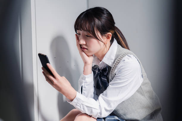 A high school girl who is depressed while looking at her phone stock photo
