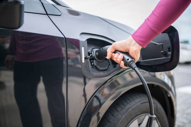 istock Midsection of man plugging cable in electric car. 1476903570