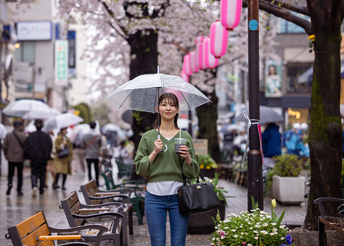 Young woman standing under cherry blossoms in city in a rainy day