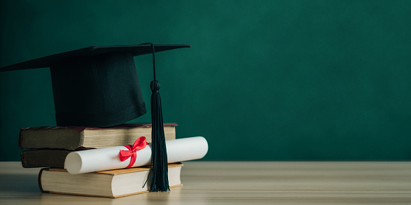 Graduation cap and diploma with a stack of books on a wood background