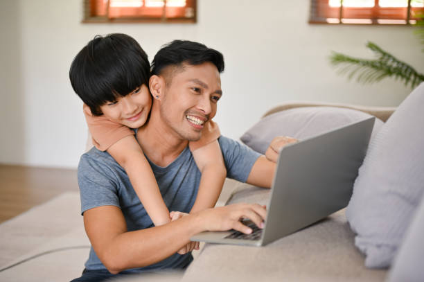 istock Cute little Asian boy hugging his father from behind while he works on his laptop 1476925873