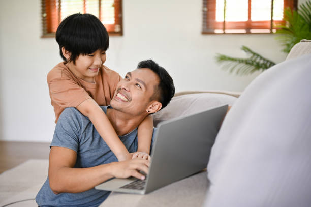 istock Cute little Asian boy hugging his father from behind while he works on his laptop 1476925890
