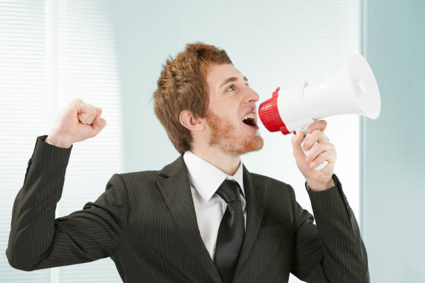 Young clerk shouting into megaphone young clerk in suit and tie with beard, shouts joyfully into a megaphone. concept of assertive and effective communication, concept of marketing and advertising, concept of being heard everywhere. spokesmodel stock pictures, royalty-free photos & images