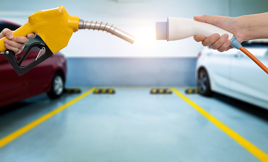 Human hands holding electric plug and gasoline nozzle