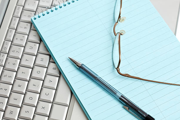 Spectacles, pen and note pad on a laptop stock photo