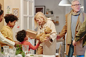 Happy mature blond woman passing teddybear to cute little grandson