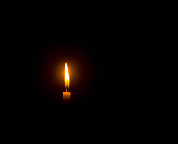 istock A single burning candle flame or light glowing on an orange candle on black or dark background on table in church for Christmas, funeral or memorial service with copy space 1476967094