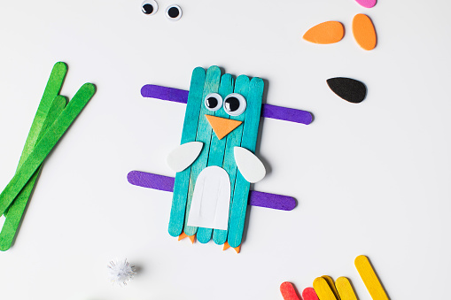 Children's funny craft made of wooden sticks and paper in the form of a bird. Children's creativity. Ideas for crafts in kindergarten.