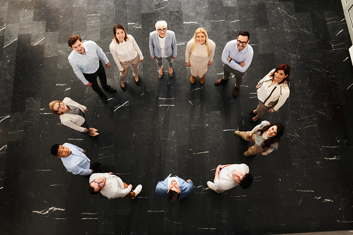 High angle view of large group of happy business colleagues standing in a circle and looking at camera. Copy space.