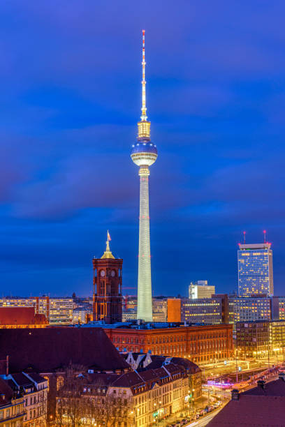 Detailed vertical image of the Berlin TV Tower (Fernsehturm) at night with the illuminated sphere and antenna against a clear dark blue sky.