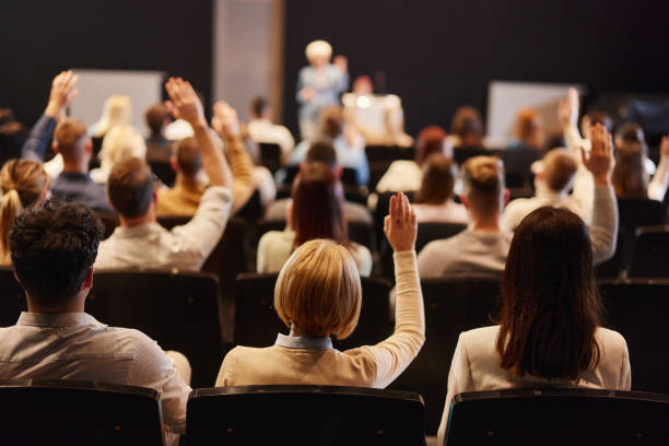 rückansicht einer menschenmenge, die bei einem seminar im kongresszentrum die hände hebt. - pressekonferenz stock-fotos und bilder