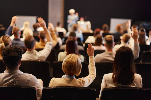 Back view of crowd of people raising hands on a seminar in convention center. stock photo