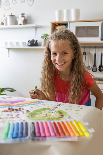 Laughing blonde curly barefoot little girl drawing paper art picture multicolored chalks sitting floor near childish hovel. Relaxed female kid happy childhood preschool early development entertainment