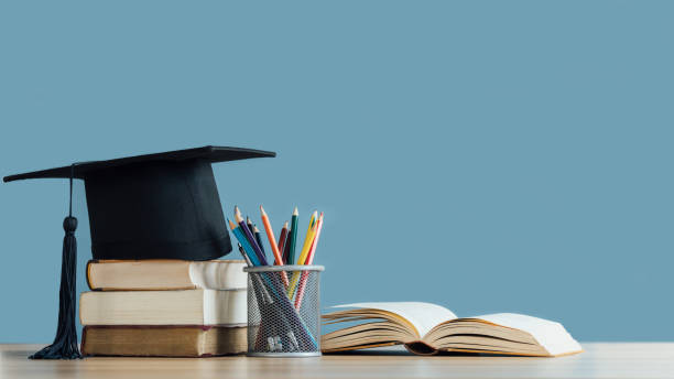 卒業式の日。青の背景に鉛筆ケースに鉛筆色の本の山にモルタルボードと卒業スクロール。教育学習のコンセプト。