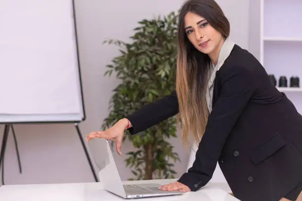 Beautiful young office woman wearing black suit is smiling at the camera while closing down her laptop
