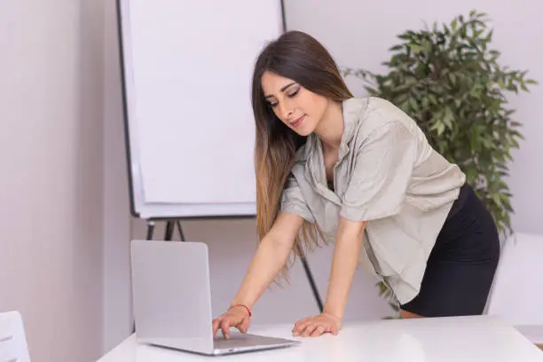 Young woman wearing black skirt is working  on her laptop as she is leaning over the table