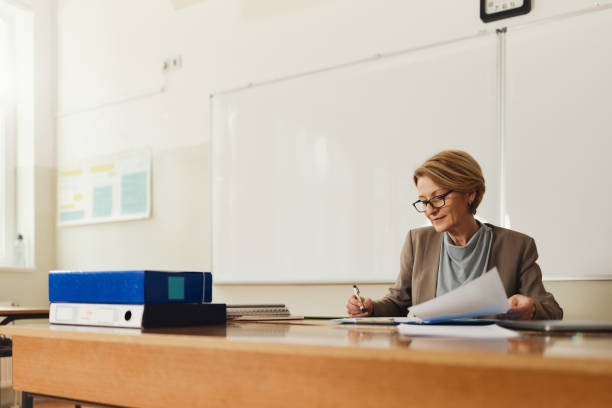 istock Senior female teacher writing her plans in the classroom. 1476981645