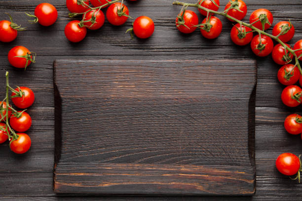 Vintage cutting board and cherry tomatoes on branches on a dark background with space for text top view.