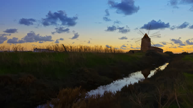 TIME LAPSE of clouds moving over traditional windmill by agricultural field. Cloudscape at Trapani, Sicily, Italy