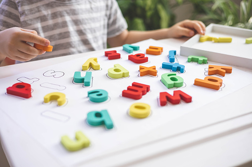 Male kid playing with wooden eco friendly alphabet letters board on table top view. Intellectual game preschool primary education early development font characters for learning reading and writing