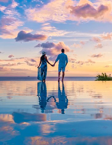 Young men and women watching the sunset with reflection in the infinity swimming pool at Saint Lucia Caribbean, couple at infinity pool during sunset with beautiful reflection