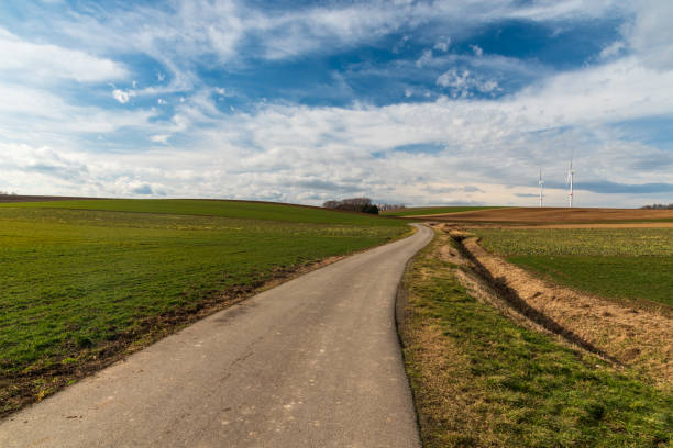 Early springtime countryside with road, fields, wind turbines and blue sky with clouds stock photo