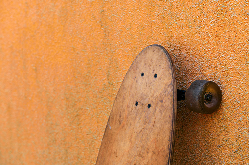 Worn skate longboard leaning against the dirty orange wall, selective focus