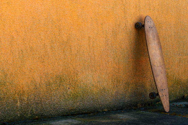 Worn skate longboard leaning against the dirty orange wall, selective focus