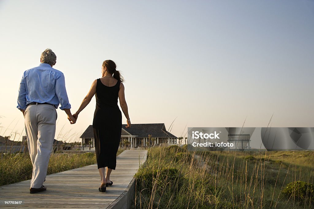 Couple on Boardwalk Couple walk hand in hand on a boardwalk towards a beach pavilion. Horizontal shot. North Carolina - US State Stock Photo